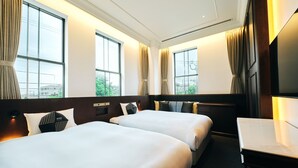 A hotel room with two beds, large windows, a desk, and a TV.