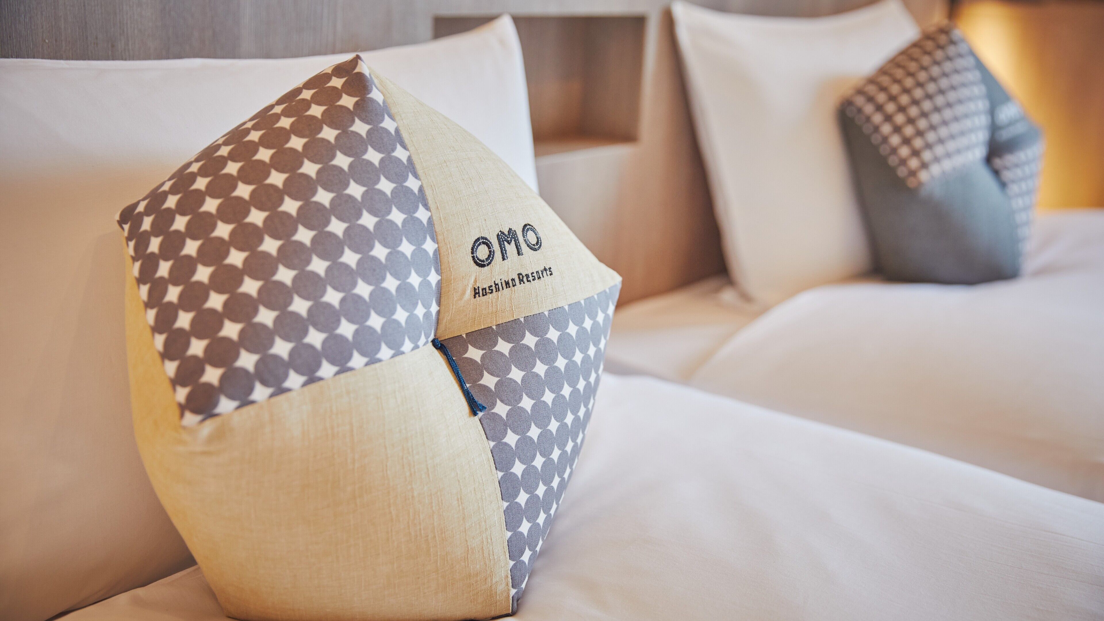 A bed with a pillow featuring a geometric pattern and the text "OMO Hashing Resorts".