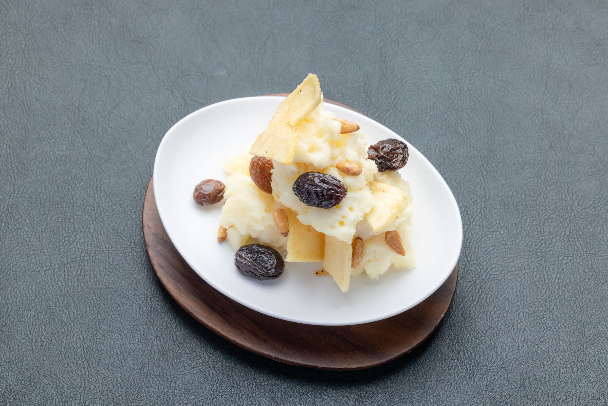 A dessert on a white plate with almonds and raisins on a dark wooden board.