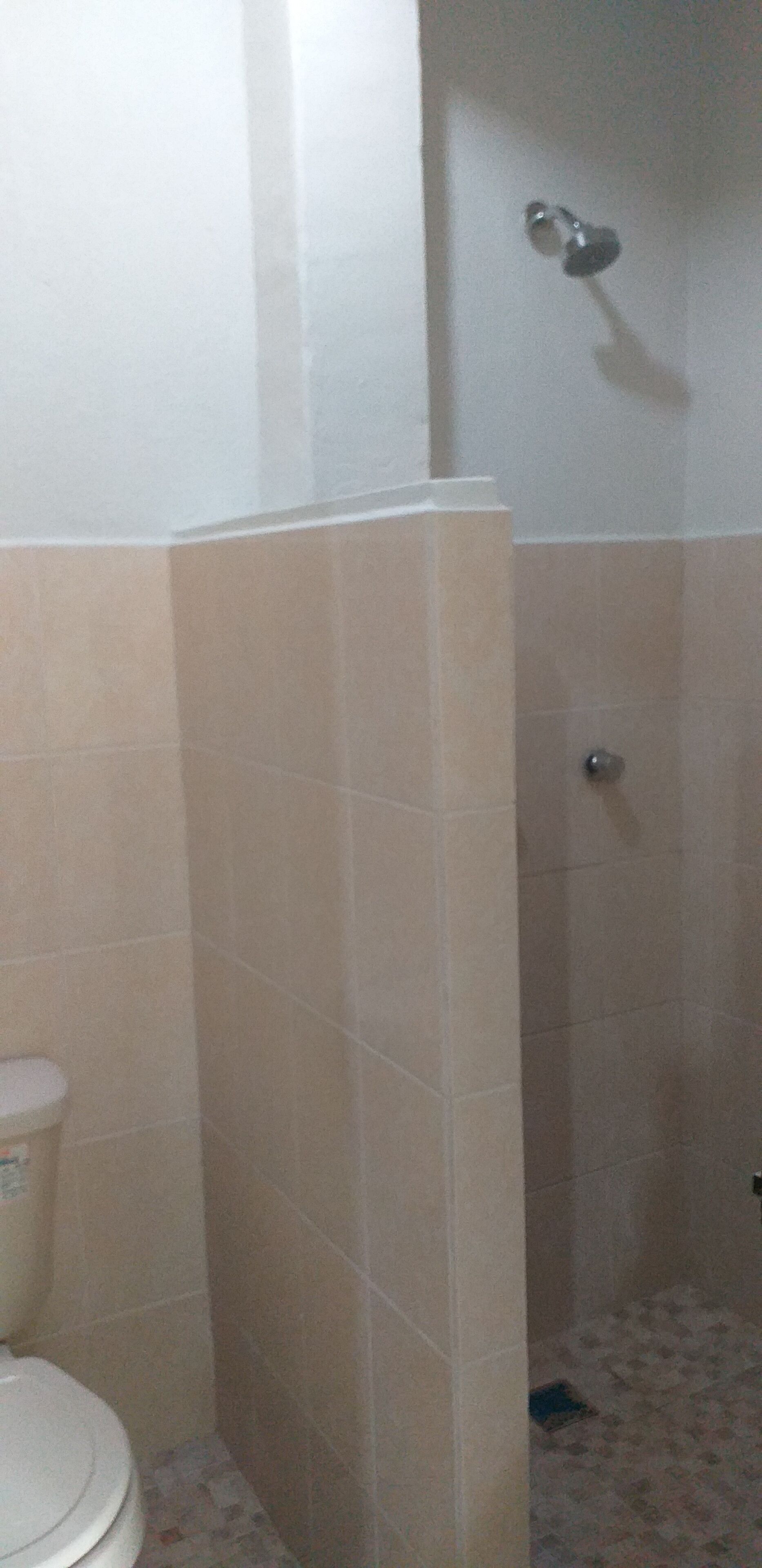 Une salle de bain avec des carreaux de couleur beige, des toilettes et un espace douche.