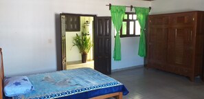 A bedroom with a bed, a wooden wardrobe, a potted plant, and a door leading to another room. - Colonial-style house (San Cristóbal de las Casas)