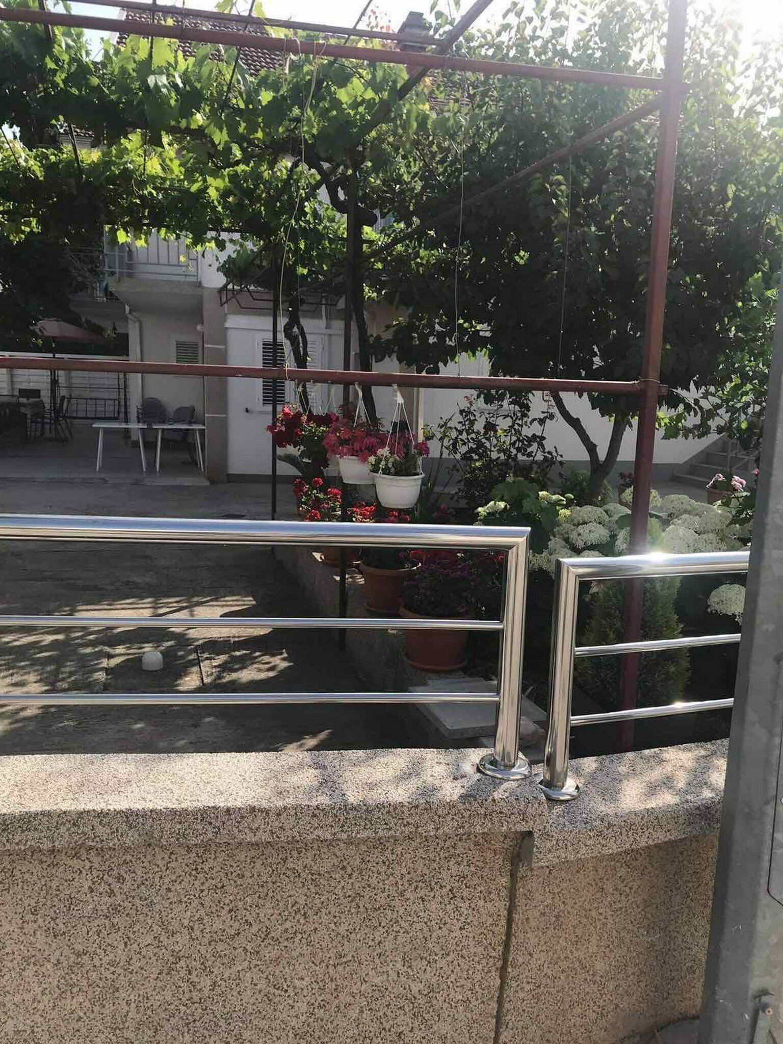 A balcony with a metal railing, potted plants, and a view of a building with a staircase.