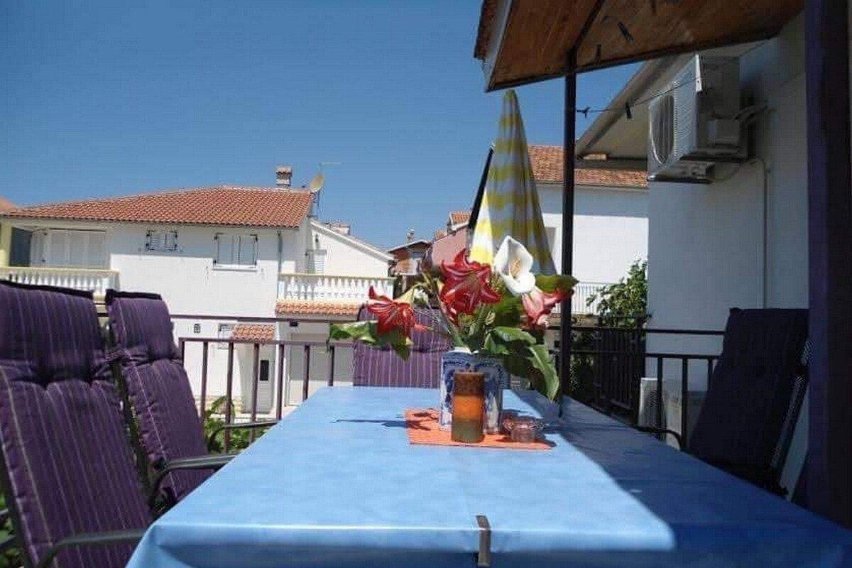 Un balcon avec une table bleue, des chaises violettes et un arrangement floral.