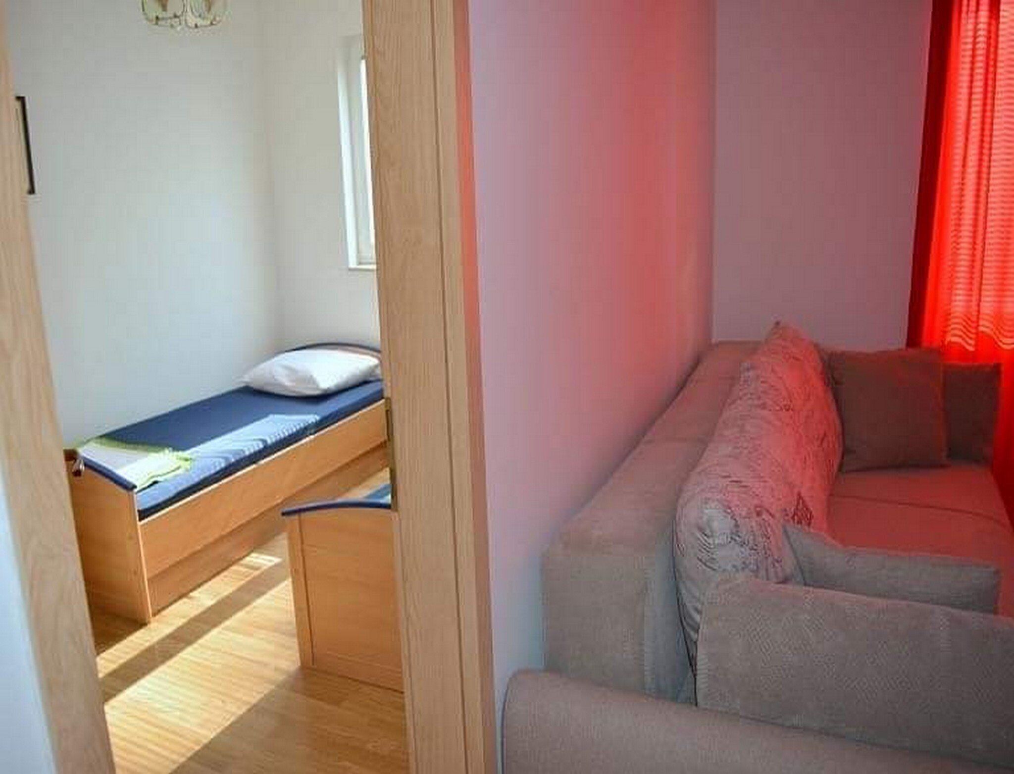 Une petite pièce comprenant un lit, un canapé et une fenêtre avec des rideaux rouges.