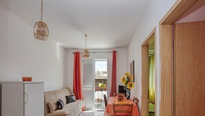 Espaço compacto com cozinha compacta, sofá, mesa de jantar com cadeiras e vista para área externa por uma porta de vidro.