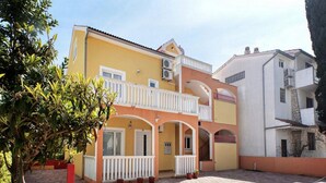 Um edifício de dois andares com fachada amarela, varandas brancas e um pátio com piso de tijolos.