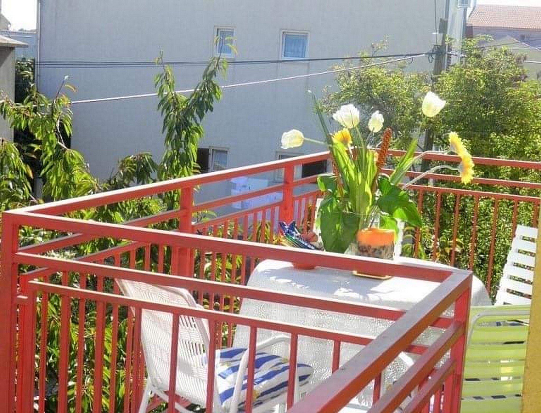 A balcony with a red railing, a white chair, and a table with a potted plant.