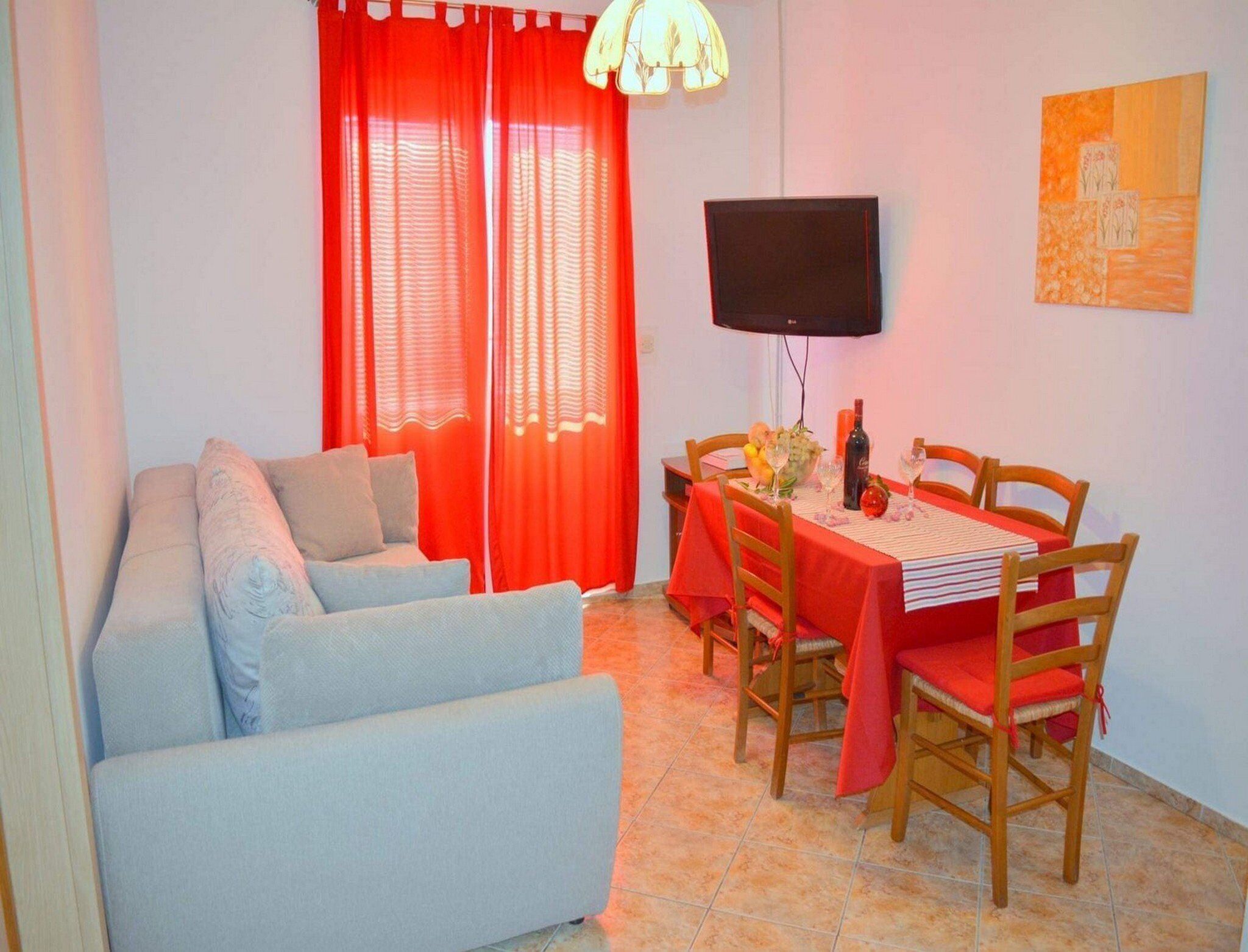 Ein Wohnzimmer mit einer Couch, einem Esstisch, Stühlen, einem Flachbildfernseher und einem Bild an der Wand.