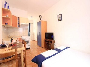 A compact hotel room with a bed, a small kitchenette, a dining table with chairs, and a television. - Apartments Villa Sarajevo (Vodice)