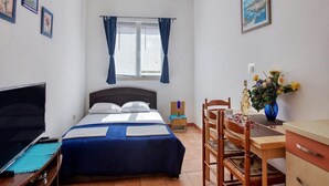 Quarto com cama, escrivaninha, cadeira, televisão e janela com cortinas.