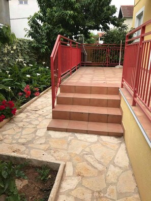 A set of stone steps leading up to a red metal railing, surrounded by greenery and a yellow wall. - Apartments Villa Sarajevo (Vodice)