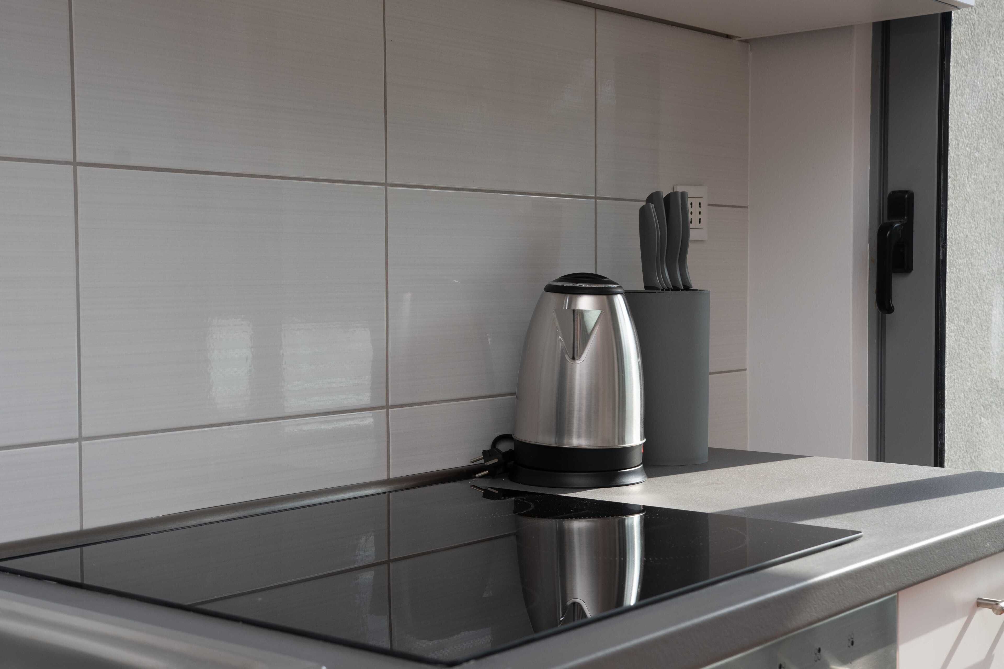 A modern kitchen with a black induction cooktop, a stainless steel kettle, and a coffee maker.
