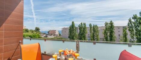 A balcony with a table set for breakfast, overlooking a body of water and buildings.