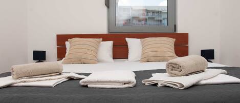 Una cama bien hecha con un edredón oscuro, dos almohadas y toallas enrolladas.