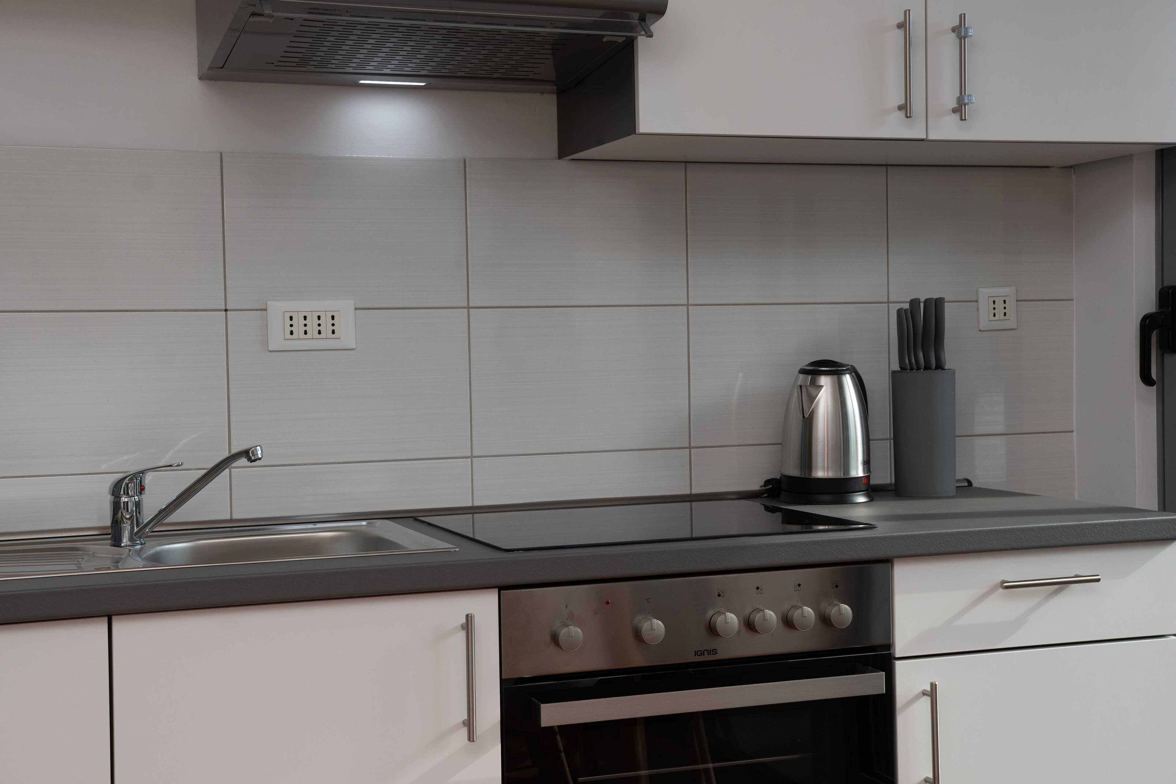 Een moderne keuken met een roestvrijstalen afzuigkap, een inbouwoven, een spoelbak met kraan en een waterkoker op het aanrecht.