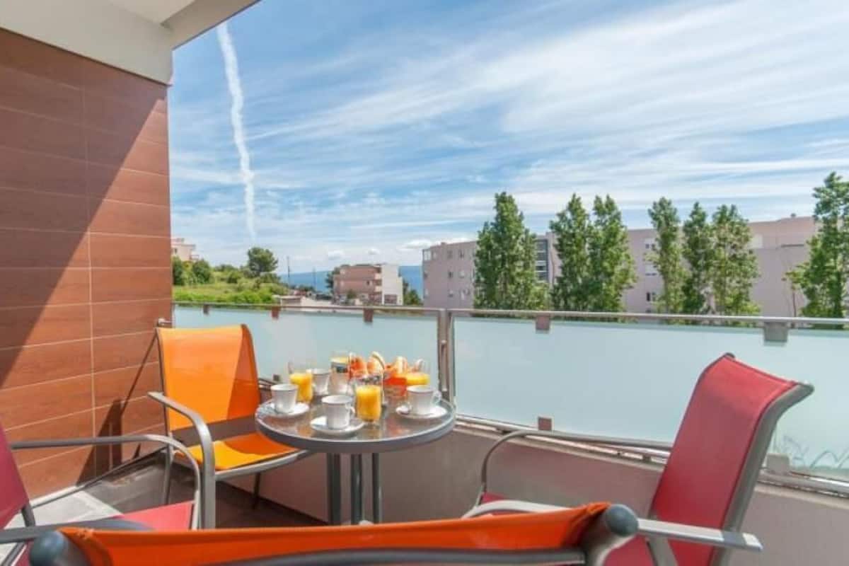 A balcony with a table set for breakfast, chairs, and a view of buildings and trees.
