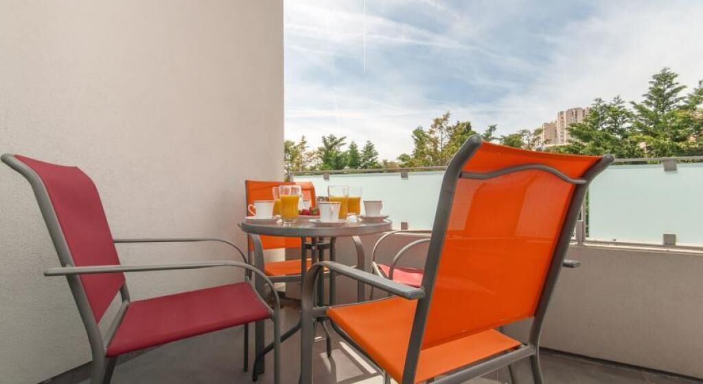 A balcony with two orange chairs and a small table with a glass of orange juice and a cup.