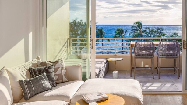 A balcony with a view of the ocean, a sofa, two chairs, and a small table.