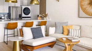 A modern living room with a sofa, two chairs, a coffee table, and a kitchen area with a washing machine.