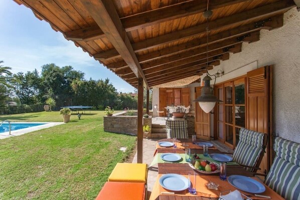 Une terrasse couverte avec une piscine, un espace repas extérieur et une vue sur le jardin environnant.
