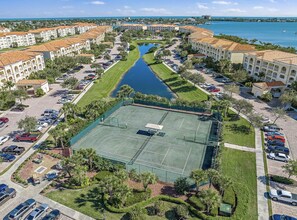 An aerial view of a residential area with a tennis court, a canal, and buildings with red-tiled roofs.