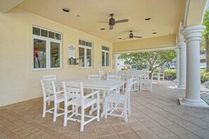 An outdoor patio with white tables and chairs, ceiling fans, and large windows.
