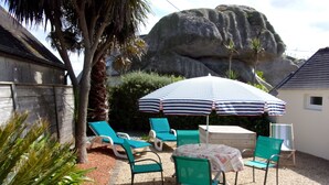 En terrasse med fire grønne liggestole og en stribet parasol, omgivet af klippeformationer og palmer.