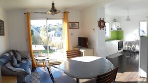 A living room with a sofa, a covered table, a television, and a view of the outdoors. - Sea view, terrace. Sleeps 4. (Fécamp)