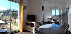 Habitación con una mesa de comedor, sillas, un televisor sobre un mueble bajo, un escritorio con silla y vistas al exterior.