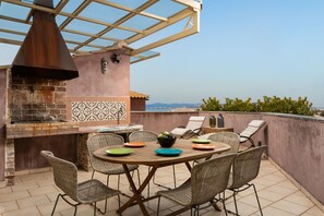 Une terrasse extérieure avec un barbecue en briques, des chaises en osier et une table dressée pour le repas.