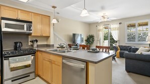 Una cocina moderna con una isla central, electrodomésticos de acero inoxidable, armarios de madera y un área de comedor con sofá y mesa.
