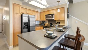 Una cocina moderna con una isla central, electrodomésticos de acero inoxidable, armarios de madera e iluminación colgante.