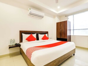 Habitación de hotel con cama, mesita de noche, equipo de aire acondicionado, armario y ventana.