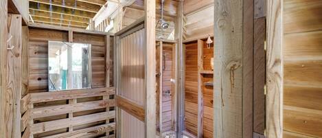 Interior de uma cabana de madeira, com um banco de madeira, uma porta de metal e uma janela.
