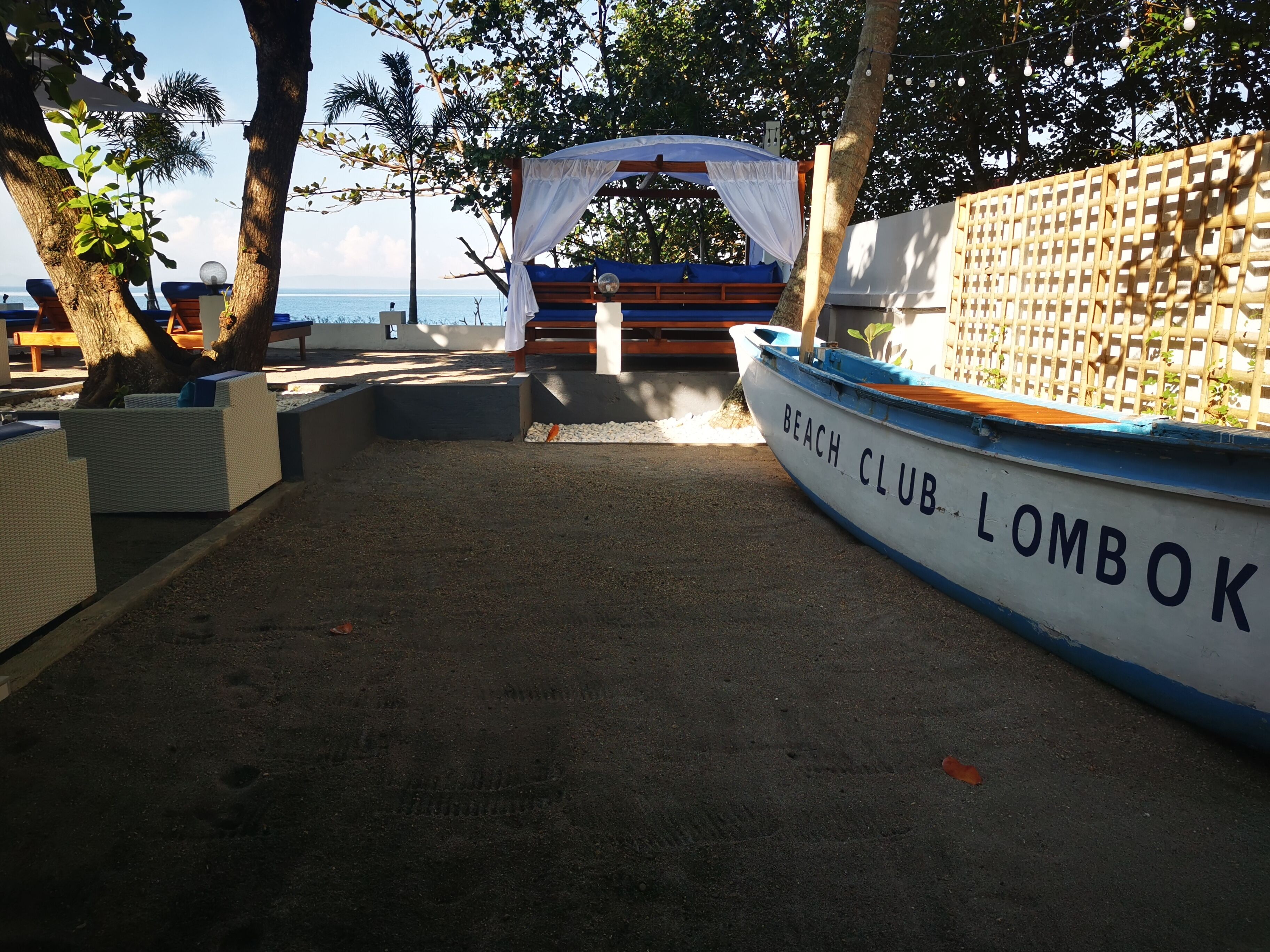 Un club de playa llamado 'Lombok' con un bote, asientos al aire libre y una pérgola.