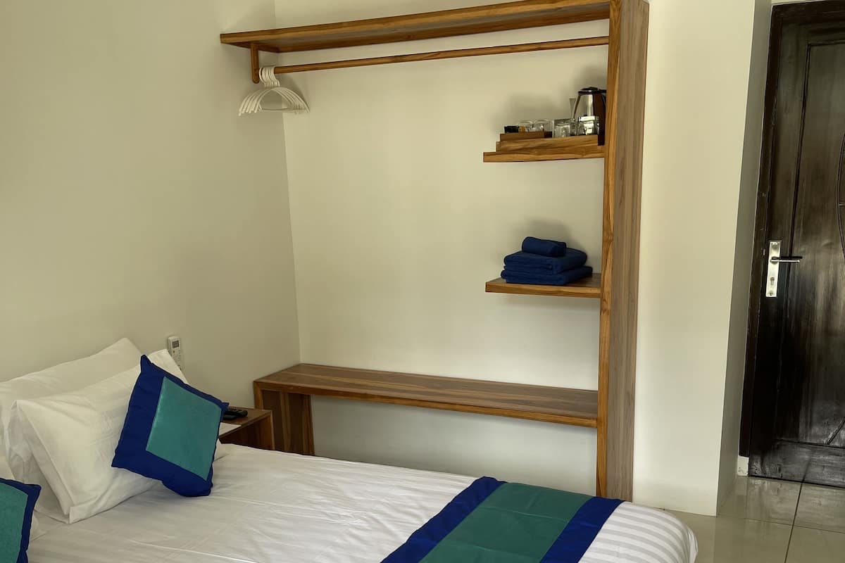 A neatly made bed with a striped bedspread, a wooden headboard with shelves, and a bedside table with a lamp.