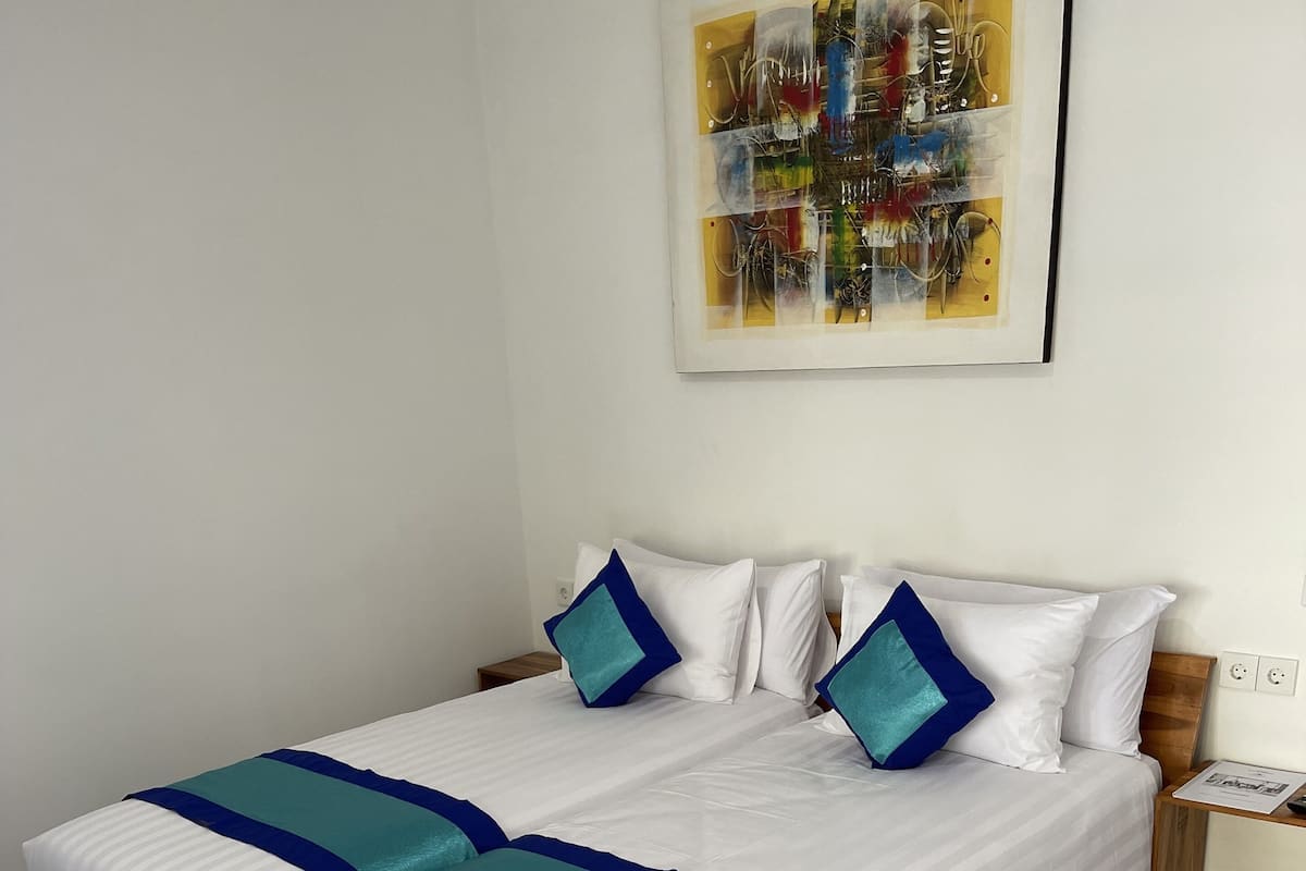 A neatly made bed with white and blue bedding, a wooden headboard, and a marble-tiled floor.