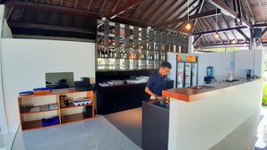 A bar area with a bartender, shelves of liquor bottles, a water dispenser, and a counter with a computer and papers. - Beach Club Lombok by Bale Solah (Senggigi)