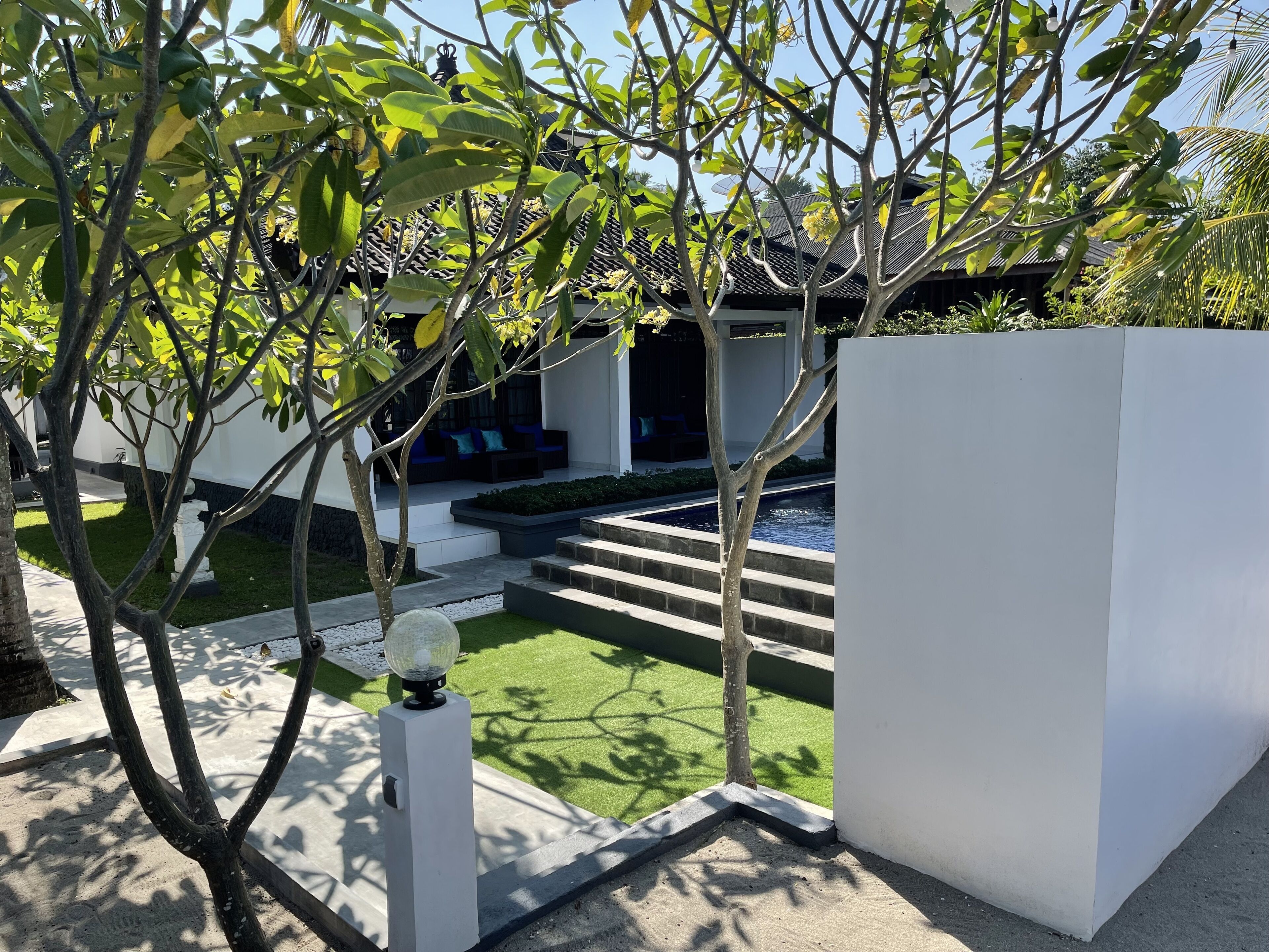 A modern outdoor area with a pool, steps leading to a covered seating area, and a white wall.