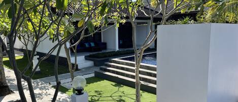 A modern outdoor area with a pool, steps leading to a covered seating area, and a white wall.