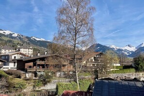 A mountain village with traditional wooden houses, a leafless tree, and snow-capped mountains in the background. - Belle Kitz urban villa for 11 with sauna & garden (Kitzbühel)