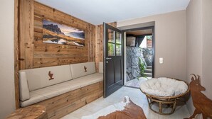 Ein Zimmer mit Holzwandverkleidung, einer Bank, einem Rattan-Sessel und einem Kuhfellteppich.