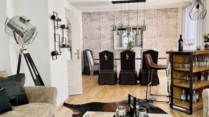 Ein modernes Wohnzimmer mit einer Couch, einem Couchtisch mit Dekoration, einem Essbereich mit Stühlen, einer Bar mit Gläsern und einer an der Wand montierten Kamera.