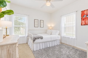 A bedroom with a bed, bedside lamps, a window with blinds, a ceiling fan, and a painting on the wall.