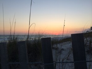 A beach scene with a wooden fence and tall grasses in the foreground.