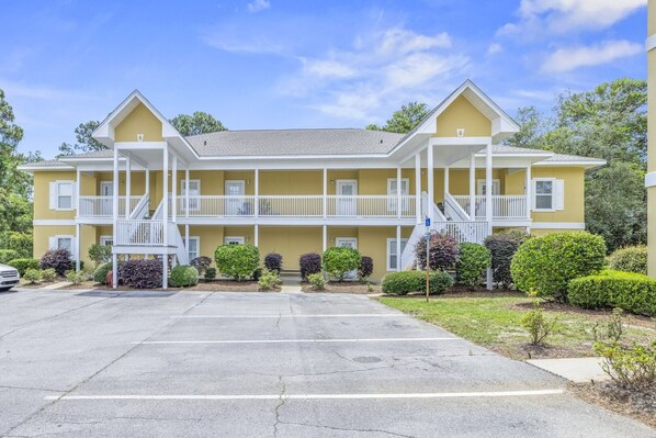 A two-story motel with a central courtyard, a parking lot, and a clear sky.