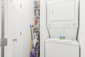 A laundry area with a washing machine, shelves with cleaning supplies, and a door.
