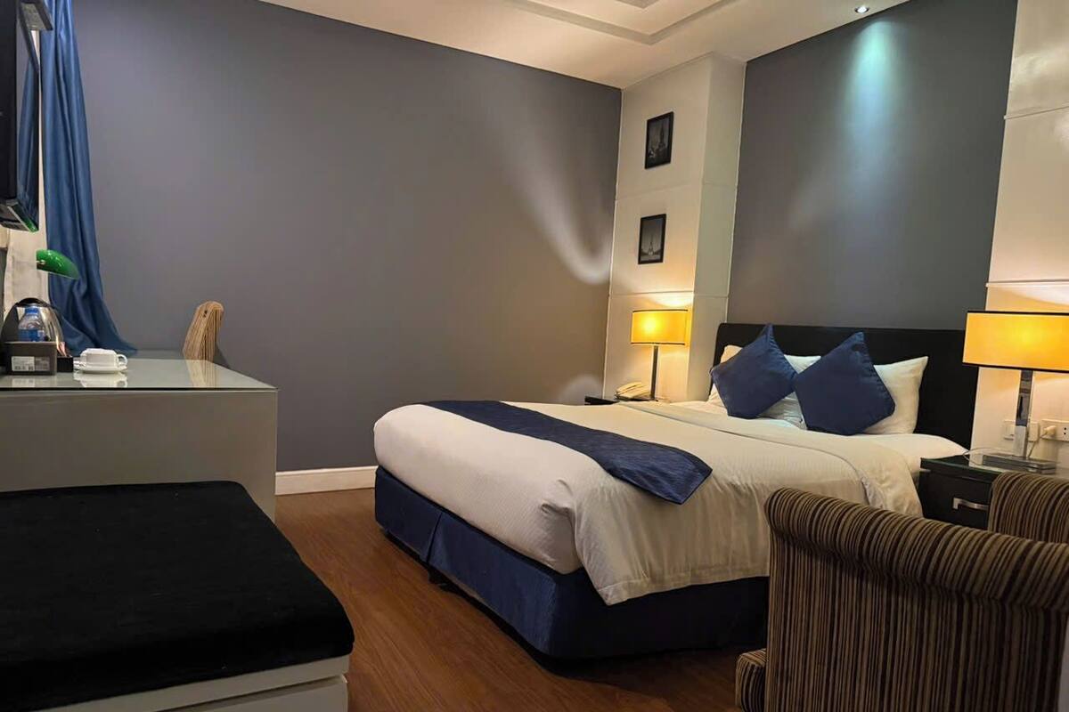 A hotel room with a bed, bedside tables, a desk, and a chair.