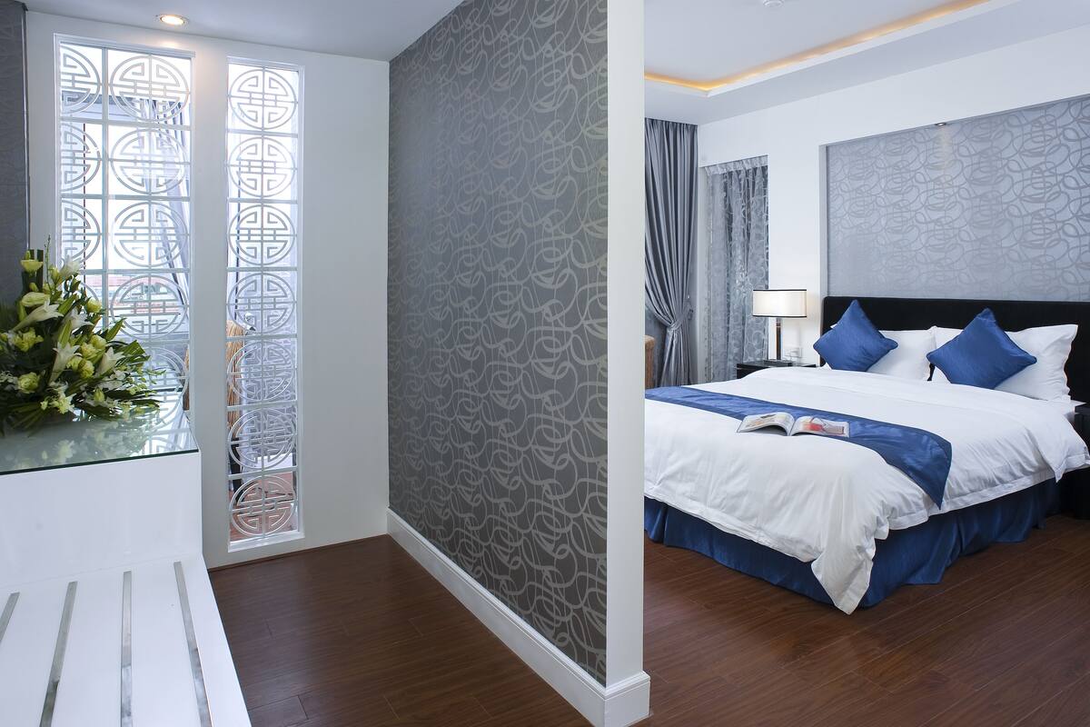 A hotel room with a bed, a nightstand, a lamp, and a window with decorative glass panels.