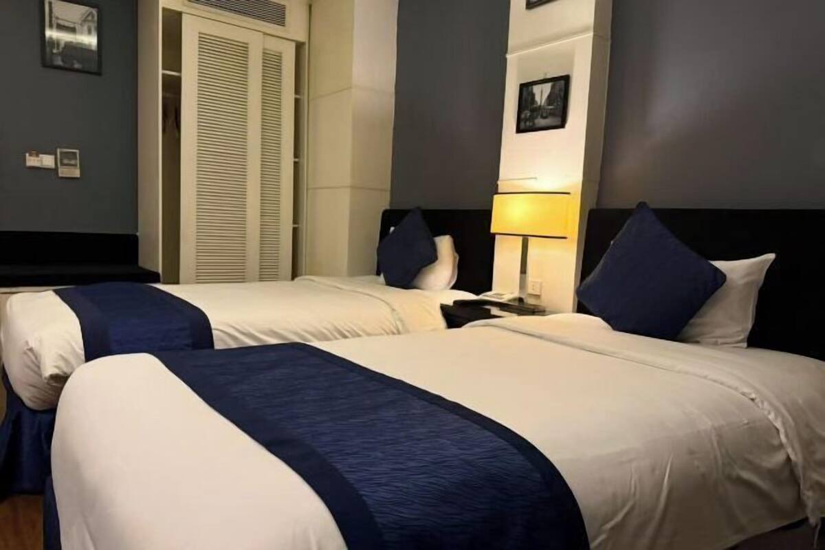 A hotel room with two beds, a nightstand, a lamp, and a closet.